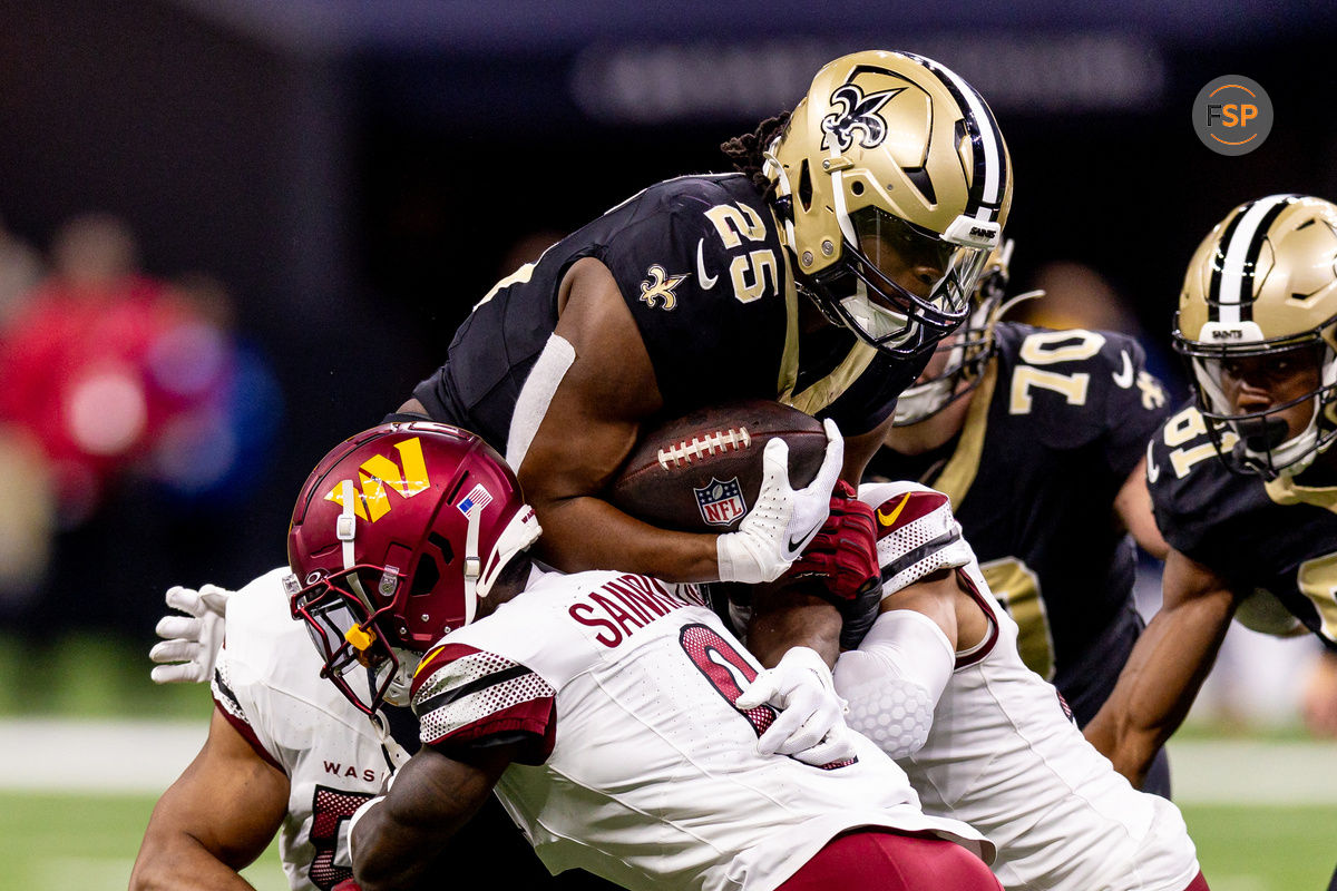 Dec 15, 2024; New Orleans, Louisiana, USA;  New Orleans Saints running back Kendre Miller (25)  is tackled by Washington Commanders cornerback Mike Sainristil (0) during the second half at Caesars Superdome. Credit: Stephen Lew-Imagn Images