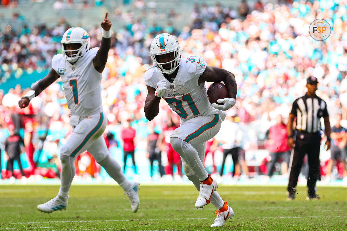 Oct 27, 2024; Miami Gardens, Florida, USA; Miami Dolphins running back Raheem Mostert (31) runs with the football for a touchdown as quarterback Tua Tagovailoa (1) celebrates during the fourth quarter at Hard Rock Stadium. Credit: Sam Navarro-Imagn Images