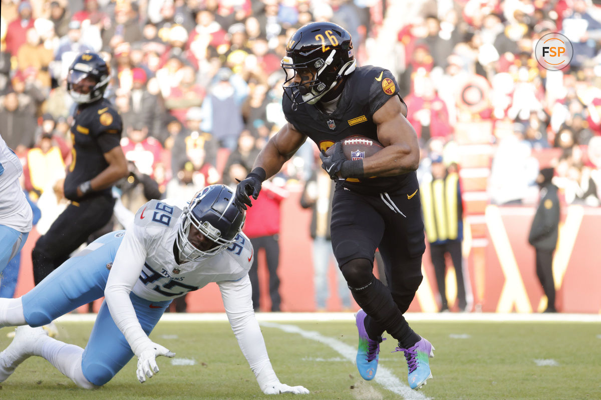 Dec 1, 2024; Landover, Maryland, USA; Washington Commanders running back Jeremy McNichols (26) carries the ball past Tennessee Titans linebacker Ali Gaye (99) during the first half at Northwest Stadium. Credit: Amber Searls-Imagn Images