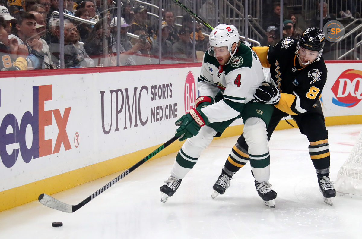 Oct 29, 2024; Pittsburgh, Pennsylvania, USA;  Minnesota Wild defenseman Jon Merrill (4) chases the puck against pressure from Pittsburgh Penguins left wing Michael Bunting (8) during the second period at PPG Paints Arena. Credit: Charles LeClaire-Imagn Images